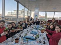 Çocuklar ve öğretmenler, seraya bitki dikimi yaparken mutlu ve öğreniyorlar.